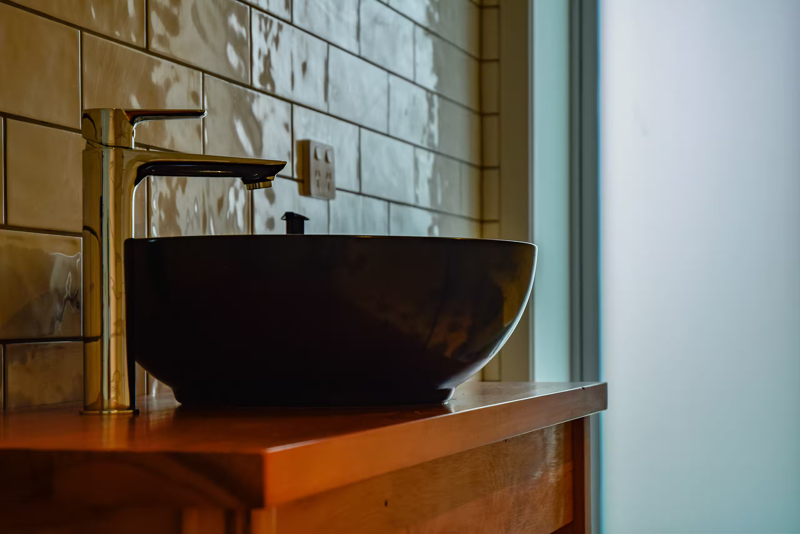 The bathroom vanity, dark vessel basin and brass tap